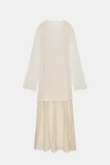 Vestido largo de punto ligero color crudo, con cuello redondo y mangas largas. Presenta un forro interior de tela satinada color beige claro que asoma en el bajo, creando un efecto de dos piezas.