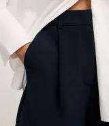 Short blanco de corte sastre, tiro alto, con pliegues frontales y trabillas en la cintura. Presenta solapas simulando bolsillos traseros.