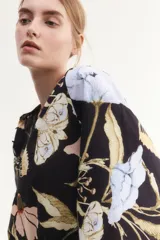 Blusa oversized de algodón y viscosa con estampado floral, cuello mao, abertura frontal con botones forrados, mangas globo largas de corte raglán con puños finos abotonados y bajo levemente redondeado.