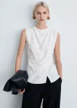 Blusa blanca sin mangas de tejido fluido con diseño cruzado y cuello redondo. Presenta cierre de cremallera en la parte posterior y detalles drapeados.