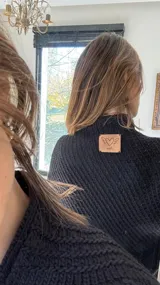 Poncho tejido en lana merino color crudo, con cuello alto y etiqueta de cuero con logo en la espalda.