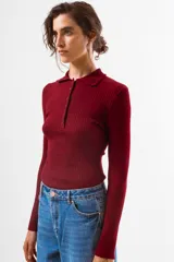 Top de tejido de punto acanalado color negro, de manga larga y cuello polo con botones frontales.