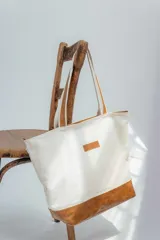 Bolso tipo tote de lona color crudo con base y asas de cuero marrón.