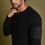 Sweater negro de punto con cuello redondo y manga larga. Presenta un bolsillo con cierre en la manga izquierda.