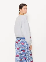 Buzo gris melange de rústico, con escote redondo, mangas largas, puños y cintura en tela complemento. Tiene un bordado de hongo y logo JCH.