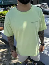 Remera color verde claro con estampado en la espalda de una ola, palmeras y montañas.
