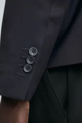 Blazer negro de corte relaxed fit confeccionada en tejido con lana. Cuello con solapas de muesca y manga larga acabada en puño con botones. Bolsillos de vivo en pecho y de solapa en cadera. Detalle de bolsillo interior. Bajo con aberturas en espalda. Cierre frontal de botonadura.