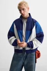 Chaqueta deportiva azul marino, azul y blanca con cierre frontal, cuello alto y bolsillos laterales.