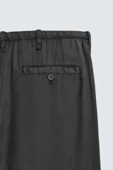 Pantalón negro de corte relajado y pierna ancha, confeccionado en mezcla de algodón y lino. Presenta cintura elástica ajustable con cordón y cierre frontal con cremallera y botón.