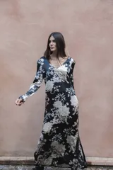 Vestido largo de seda color negro con estampado de flores blancas, palmeras y tigres. Tiene escote en V, mangas largas y lazo en la espalda.