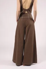 Pantalón negro de tiro alto, corte ancho y largo, con pliegues frontales y pespuntes contrastantes en blanco en la cintura y bolsillos.