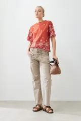 Remera color ladrillo con bordado de flores blancas en el ruedo y las mangas.