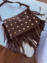Bandolera de gamuza marrón chocolate con tachas doradas y flecos. Tiene correa de gamuza extraíble y otra de cadena dorada.