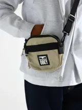 Bolso bandolera pequeño color arena con detalles en negro y logo de Obey estampado en blanco. Tiene correa ajustable y cierre de cremallera.