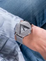 Reloj Guess para dama con malla metálica plateada, caja redonda con cristales incrustados y logo triangular de la marca en el centro.