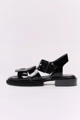 Sandalias bajas de cuero charolado color negro, con tiras anchas cruzadas y hebilla cuadrada.