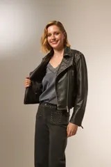 Chaqueta corta de cuero sintético negro con cuello solapa, cierre frontal asimétrico, bolsillos con cierre y tachas plateadas en cuello y hombros.