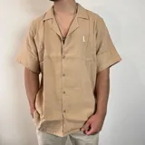 Camisa color beige de muselina con cuello solapa, manga corta y corte oversize.