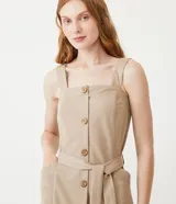 Vestido midi color beige con breteles anchos, escote cuadrado, botones frontales, bolsillos laterales y cinturón de tela con hebilla.