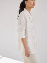 Camisa negra de lino con corte femenino, cuello clásico, cierre frontal con botones y mangas 3/4 con puños enrollados. Presenta detalles de frunces verticales en el frente y bolsillos de parche a la altura de la cadera.