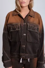 Campera de denim marrón con efecto degradado, corte boxy, cuello camisero, cierre frontal con botones metálicos, mangas largas con puños abotonados, dos bolsillos frontales con solapa y parche con logo en el frente.