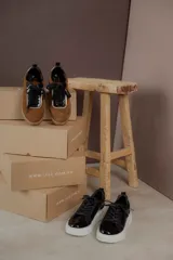 Championes marrones de cuero con cordones negros, puntera de charol y detalles dorados.