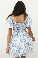 Vestido corto blanco con estampado floral azul, escote cuadrado con volados, mangas cortas abullonadas con elástico y cintura elastizada.