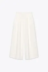 Pantalón blanco de tiro alto con pinzas delanteras, bolsillos laterales y pernera ancha. Cierre lateral con cremallera oculta.