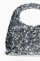 Cartera de mano plateada cubierta de lentejuelas, con asa corta y forro interior.