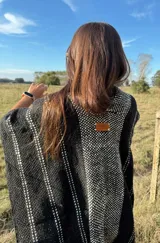 Ruana tejida a mano en telar, confeccionada en lana Merino color negro con detalles en blanco y flecos blancos.