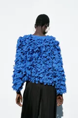 Chaqueta azul con cuello redondo y manga larga, con apliques de pétalos en toda la prenda y cierre frontal con botón a presión oculto.