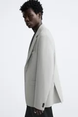 Blazer straight fit color gris claro confeccionado en tejido con viscosa. Tiene cuello con solapas de muesca, manga larga acabada en puño con botón, bolsillo de vivo en pecho, bolsillos de plastrón en cadera y bajo con aberturas en espalda. Cierre frontal de botonadura.