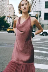 Vestido midi color lila, de cuello halter y sin mangas. La parte superior es de tejido arrugado y la falda es plisada. Tiene abertura en la espalda con cierre de botones ocultos.