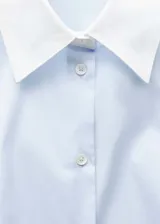 Camisa celeste de popelina de algodón con cuello y puños blancos en contraste, manga larga con puños abotonados, corte recto, cierre frontal con botones y diseño entallado.