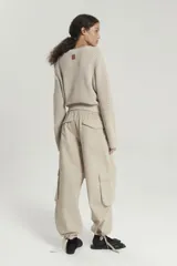 Pantalón tipo babucha color beige de gabardina liviana con cintura elástica en espalda y tira regulable en delantero. Bolsillos en diagonal con bolsa pespunteada en delantero. Bolsillos 3D plaqué en pierna delantera con tapa. Tira regulable en botamanga. Bolsillos plaqué con tapa en trasero.