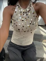 Top blanco de tejido de punto con cuello halter y espalda descubierta. Decorado con apliques de lentejuelas plateadas y doradas.