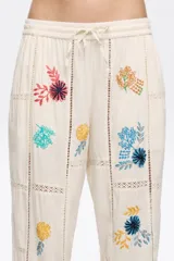 Pantalón de corte recto color crema con bordados florales multicolores.
