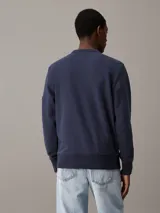 Buzo azul marino de algodón con cuello redondo y ribete en V. Tiene puños y dobladillo acanalados, y una insignia con el monograma de Calvin Klein en la manga.
