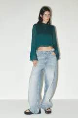 Camisa verde esmeralda de cuello alto y manga larga con volantes en los puños. Cierre en la espalda con abertura y botones.