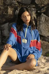 Hoodie azul de toalla con capucha, mangas largas y diseño color block con franja roja y ribete amarillo en el pecho. Logotipo bordado en el frente y bolsillos laterales.