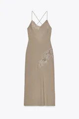 Vestido midi color beige de estilo lencero, con escote en V, tirantes finos cruzados en la espalda y detalle de bordados florales a tono en el escote y lateral.