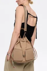 Mochila shopper de nylon color beige, con doble asa de mano, tiras ajustables y dos bolsillos frontales con cierre.