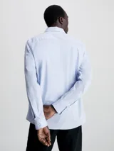 Camisa celeste de popelín de algodón elástico, corte slim, con cierre frontal de botones, mangas largas y monograma de Calvin Klein bordado en el pecho.
