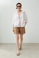 Blusa blanca de corte holgado con bordados de estrellas y detalles geométricos en color coral.