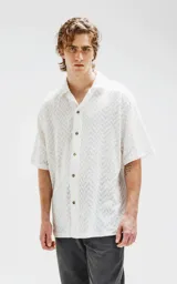 Camisa blanca de manga corta con textura calada y cierre con botones marrones.