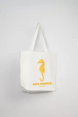Bolso de mano tipo tote bag color blanco con estampa de caballito de mar color naranja y texto "Sea Horse The Sea Capsule".