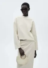 Buzo color crudo de tejido bouclé, con cuello perkins y mangas largas. Sin cierre y con terminaciones de canalé.