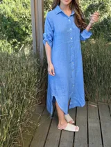 Vestido camisero largo celeste de lino, con cuello clásico, abotonadura frontal completa, mangas 3/4 con trabillas y aberturas laterales en el bajo.