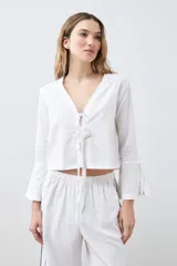 Blusa blanca de lino con escote en V y cierre frontal con lazos. Mangas largas acampanadas.
