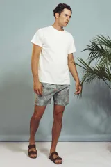 Short de baño con estampado de hojas en tonos grises y celestes, con cordón ajustable en la cintura y detalle de franja lateral con rayas rojas, blancas y negras.